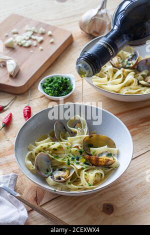 cuocete inriconoscibile versando olio d'oliva nel recipiente con gli spaghetti e. vongole poste su tavolo di legno nel ristorante Foto Stock