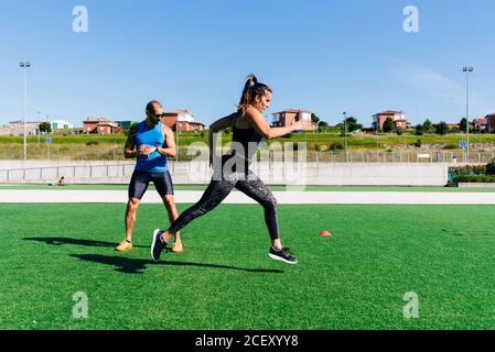 Il corpo pieno di una giovane atleta determinata che corre velocemente prato verde con coni di addestramento mentre si esercita con personal coach allo stadio Foto Stock