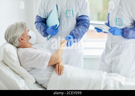 Due medici che indossano tute di protezione con guanti che esaminano la salute di paziente anziano nel reparto di malattie infettive Foto Stock