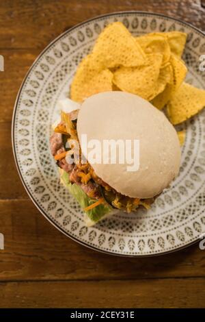 Primo piano di gustosi hamburger con cotoletta di pollo e verdure varie su piatto posto su tavolo di legno in cucina Foto Stock