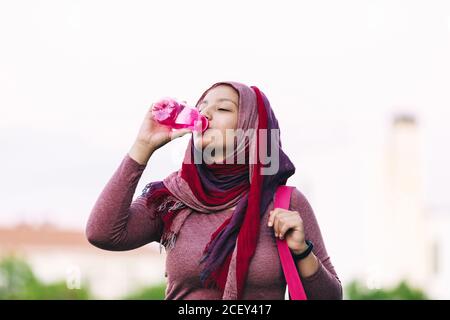 Atleta araba in hijab e abbigliamento attivo in piedi via e godendo di acqua fresca dopo l'allenamento Foto Stock