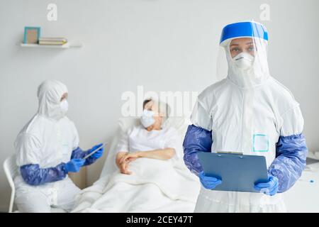 Due medici professionisti che indossano tute di protezione con guanti, maschere e occhiali che lavorano con pazienti anziani nel reparto di malattie infettive Foto Stock