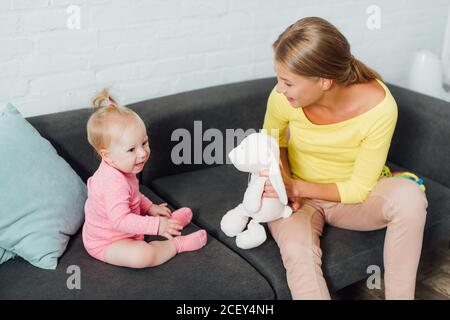 Donna che tiene il giocattolo morbido mentre gioca con la figlia del bambino dentro soggiorno Foto Stock