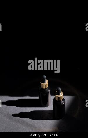 Pipettare il flacone contagocce in vetro nero con elementi dorati sul sfondo scuro Foto Stock