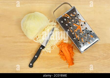 Ingredienti di coleslaw, cavolo bianco e carote su un tagliere con un coltello e una grattugia Foto Stock