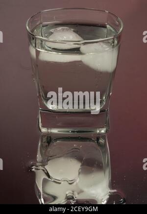 Barman versando la vodka congelata da una bottiglia in due bicchieri da shot con cubetti di ghiaccio su sfondo nero. Foto Stock