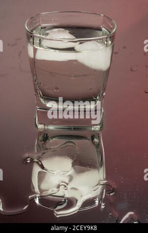 Barman versando la vodka congelata da una bottiglia in due bicchieri da shot con cubetti di ghiaccio su sfondo nero. Foto Stock