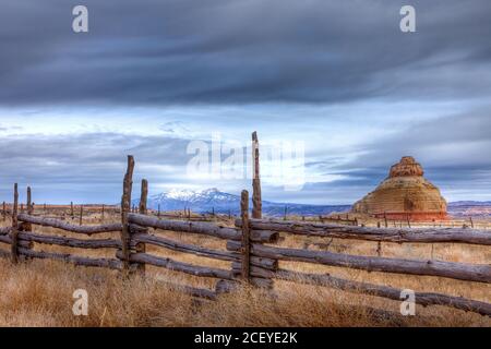 Cieli tempestosi su Church Rock e le montagne di la SAL dietro un vecchio cortale di bestiame con recinzione in legno nel sud-est dello Utah. Foto Stock