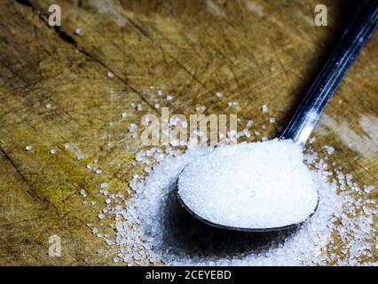 un cucchiaio di zucchero granulato su uno sfondo di legno Foto Stock