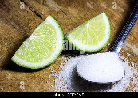 un cucchiaio di zucchero granulato e fette di lime su uno sfondo di legno. Foto Stock