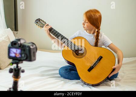 ritratto di bambina dolce blogger studiare accordi in chitarra acustica, si siede a casa, godere di suonare la chitarra. autodidatta blogger girl record video Foto Stock