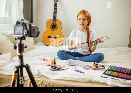 piccolo blogger di bellezza caucasica sedersi di fronte alla macchina fotografica, mostrare nuovi cosmetici decorativi, vuole fare trucco, girl registrare video su fotocamera professionale Foto Stock