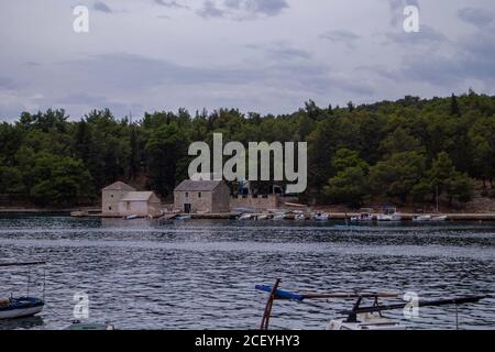 Stari Grad/Croazia-7 agosto 2020: Piccole case in pietra nella baia di Stari Grad sul bordo della pineta, ora utilizzato come stiva per attrezzature navali e stoccaggio Foto Stock