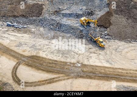 Foto drone - l'escavatore carica pietre pesanti e detriti sul dumper industriale. Le pietre vanno dalla montagna esplosa al sito di costruzione libero Foto Stock