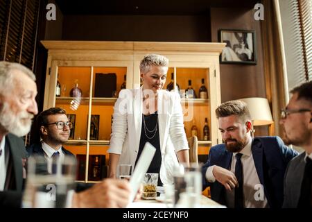 Team di colleghi che fanno una grande discussione aziendale in un ufficio moderno. Un giovane e splendido dirigente si erge con cura sul banco conferenze di fronte a me Foto Stock