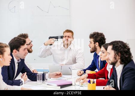 gruppo di giovani uomini d'affari caucasici in carica, giovani uomini d'affari che guardano depressi e preoccupati di lavorare in una meetina, tenendo in mano la pistola, Foto Stock