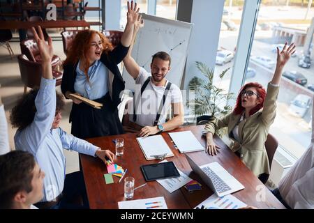 Risoluzione dei problemi in un'unica squadra. Giovane squadra caucasica di uomini e donne che lavorano insieme mentre si siedono al loro posto di lavoro in ufficio, godere Foto Stock