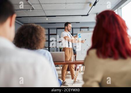 Mentore maschile leader esecutivo parlando durante il briefing, lavoratori multietnici impegnati in formazione aziendale seduta attentamente ascoltare Foto Stock