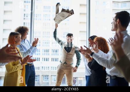 I giovani imprenditori celebrano la vittoria del loro collega arabo che si trova al centro in posa del vincitore, sfondo della finestra panoramica Foto Stock