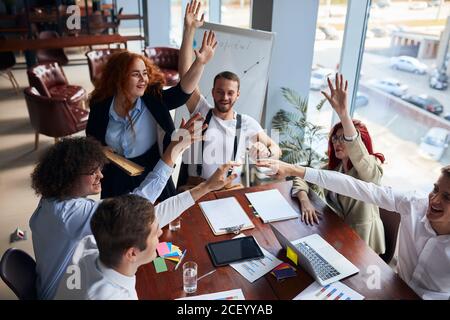 Un gruppo felice di colleghi si è Unito a mani unite per concludere una riunione di affari di successo nell'ufficio della conferenza, nei documenti, nelle matite colorate sul tavolo. Crea Foto Stock