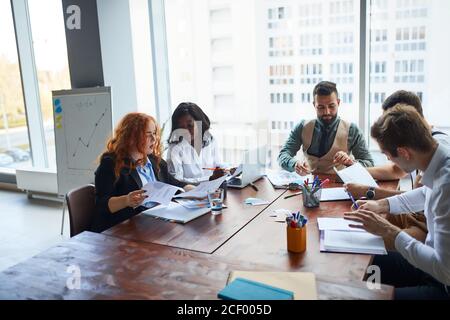 gruppo internazionale di persone, team aziendale riuniti sul tavolo per discutere le idee aziendali, utilizzando documenti, diagrammi. Persone creative di affari Foto Stock
