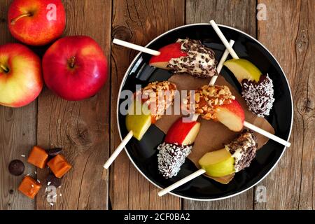 Piatto di caramello dolce misto e fette di mela ricoperti di cioccolato, scena a soffitto su legno rustico Foto Stock