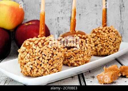 Mele autunnali al caramello con noci su un piatto con rustico sfondo di legno bianco Foto Stock