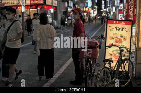 Un addetto alla consegna del cibo si trova sul lato di una strada trafficata vicino alla stazione di Kichijoji a Tokyo, Giappone Foto Stock