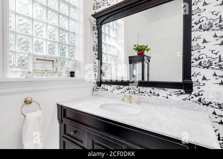 Un bagno in bianco e nero ristrutturato con carta da parati, lavandino nero, piastrelle decorative sul pavimento e piastrelle della metropolitana nella doccia. Foto Stock