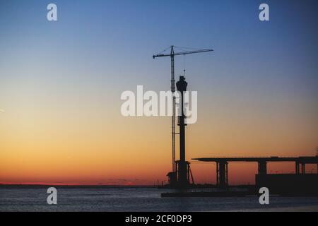 Una parte incompiuta della strada o del ponte autostradale, al tramonto o al tramonto, gru industriali e silhouette di costruzione all'alba, luce posteriore costr Foto Stock