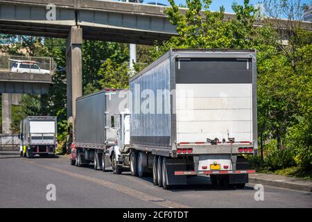 Diversi autocarri diesel industriali Big RIGs potenti per il trasporto di merci professionali con semirimorchi a secco parcheggiati sulla strada sotto strada di sorpasso int Foto Stock