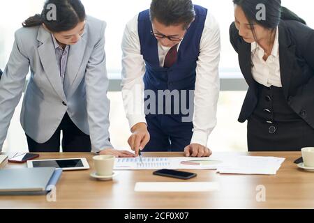 il team di dirigenti aziendali asiatici si riunisce per analizzare le prestazioni aziendali in ufficio Foto Stock