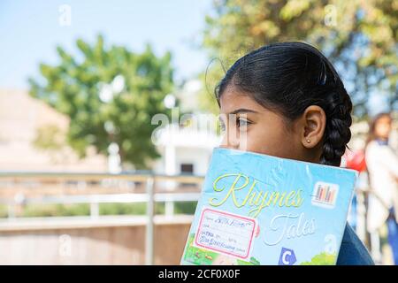 Jodhpur, Rajasthan, India - 10 gennaio 2020: Closeup della ragazza felice indiana della scuola di studente che tiene il notebook di esercitazione copre la sua faccia, in piedi all'aperto, poliziotto Foto Stock