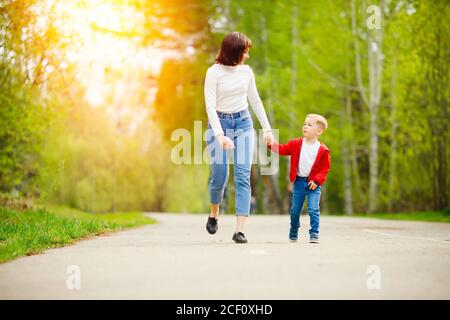 Felice famiglia caucasica madre e figlio bambino camminare nel parco, ridere e gioire, luce del sole Foto Stock