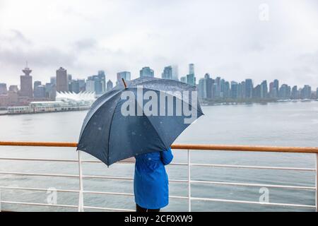 Donna di lusso in crociera di viaggio che lascia il porto guardando lo skyline della città di Vancouver sotto la pioggia con ombrello. Destinazione della nave in autunno. Foto Stock