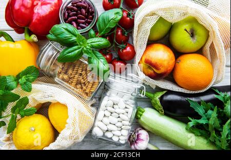 Frutta fresca e verdura in sacchetti di cotone eco sul tavolo in cucina. Mele, fagioli, pomodori, rucola, insalata dal mercato. Zero rifiuti negozi conc Foto Stock