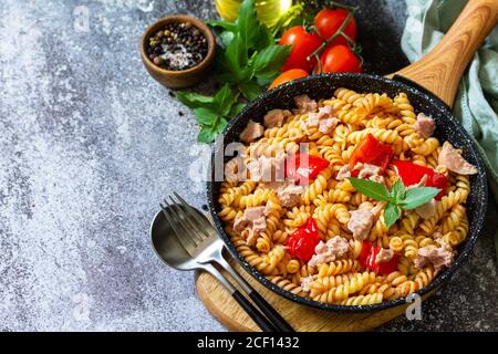 Pranzo sano. Fusilli con tonno in scatola, peperoni rossi alla griglia e pomodori in padella su un piano di pietra. Spazio di copia. Foto Stock