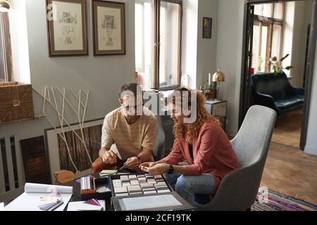 Due progettisti seduti al tavolo che esaminano piccoli pezzi di ceramica e scelta del colore per il nuovo progetto Foto Stock