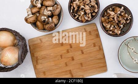 Primo piano su un tavolo da cucina i funghi bruni freschi e crudi biologici e la cipolla gialla. Cottura, ingredienti, ricetta vegetariana Foto Stock