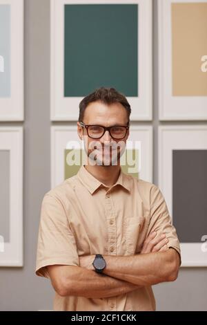 Ritratto di giovane designer moderno in occhiali in piedi con le braccia incrociato e sorridente alla fotocamera Foto Stock