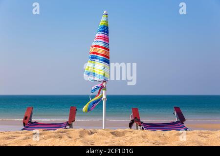 Ombrellone colorato con sedie sulla spiaggia con mare blu Foto Stock
