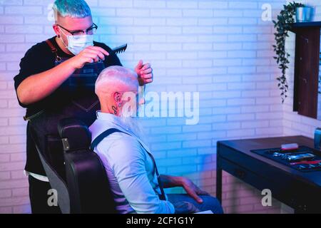 Hipster uomo anziano ottenere un taglio di capelli in un barbiere retrò Negozio durante l'epidemia di coronavirus - Focus sul cliente Foto Stock