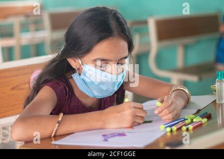 Ragazzina in maschera medica impegnata nel disegno schizzo in classe - concetto di sicurezza murature a scuola a causa di coronavirus o covid-19 pandemia. Foto Stock