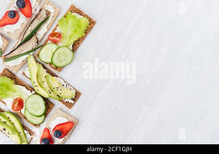 Sano assortimento dietetico di patatine toast piatti di segale con verdure fresche, frutta matura, conserve di pesce, formaggio crema su sfondo di legno bianco, vie superiore Foto Stock