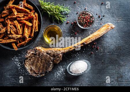 Bistecca di manzo tomahawk alla griglia con patate dolci fritte spezie al sale olio d'oliva e rosmarino su tavola rustica - cima di visualizza Foto Stock