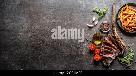 Fette di manzo grigliate con bistecca di tomahawk e patatine fritte dolci spezie saline olio d'oliva e rosmarino su tavola rustica - vista dall'alto Foto Stock