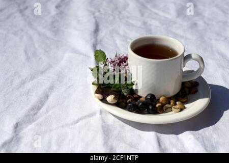 Composizione del caffè con tazza bianca di caffè con erbe e fagioli di caffè, cioccolato, bacca, menta su tavola di lino come sfondo Foto Stock