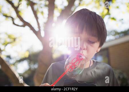 Ragazzo che soffia bolle in cortile soleggiato Foto Stock