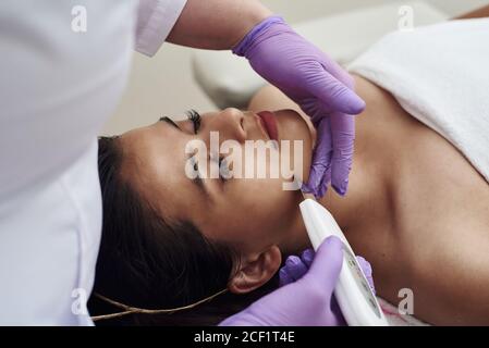 Donna che riceve la terapia di pulizia con un'apparecchiatura professionale ultrasonica in ufficio di cosmetologia. Procedura di pulizia a ultrasuoni del viso. Clinica cosmetologica. Foto Stock