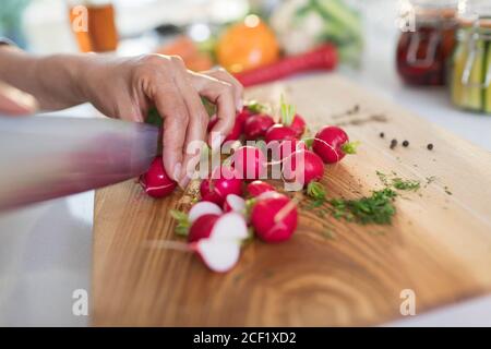 Primo piano donna che affetta ravanelli freschi sul tagliere Foto Stock